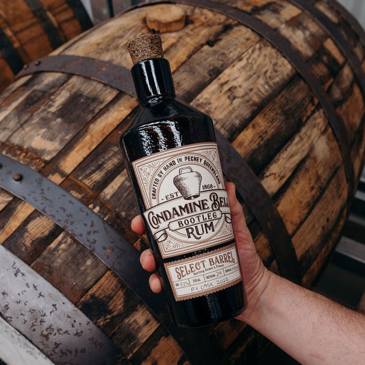 Bottle of Cynamine Bee Bottler Rum held in front of a wooden barrel