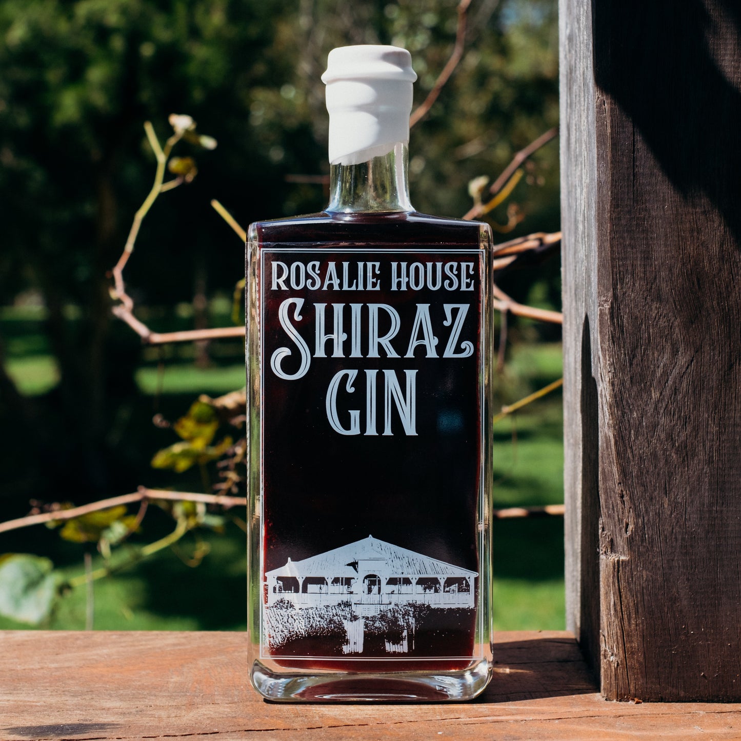 Bottle of Rosalie House Shiraz Gin on a wooden surface with a blurred natural background